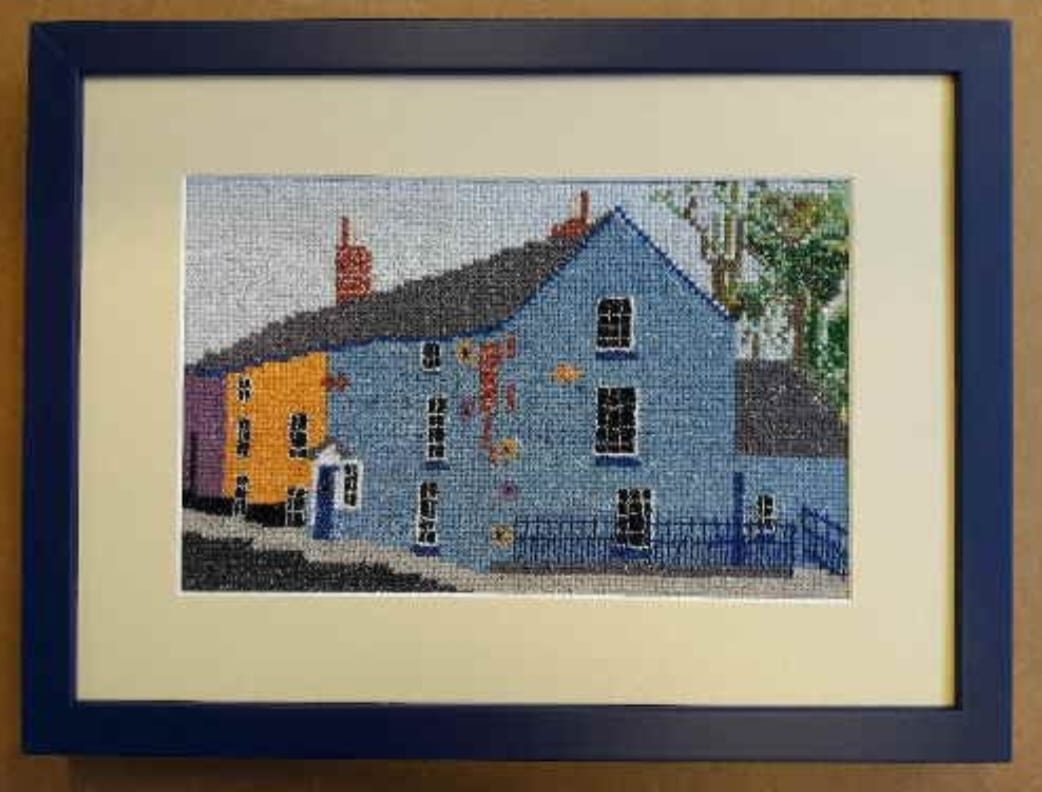 A stitched cottage, spaced off the glass in a navy box frame with a cream mount.
